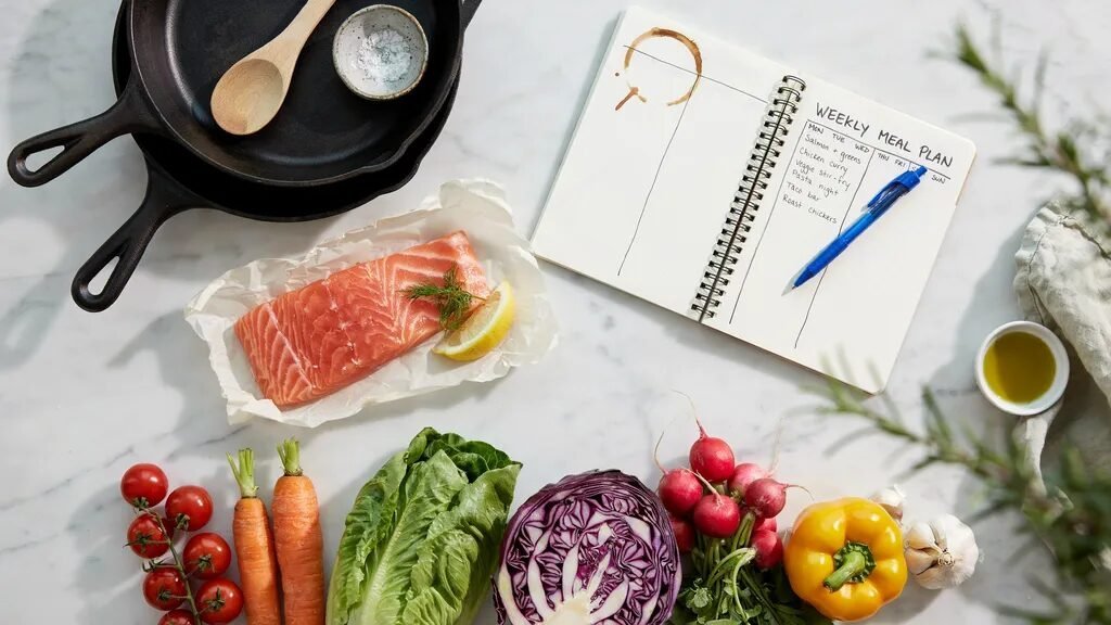 Salmon fillet, red cabbage, carrots, peppers, and radishes next to a handwritten weekly meal planner.
