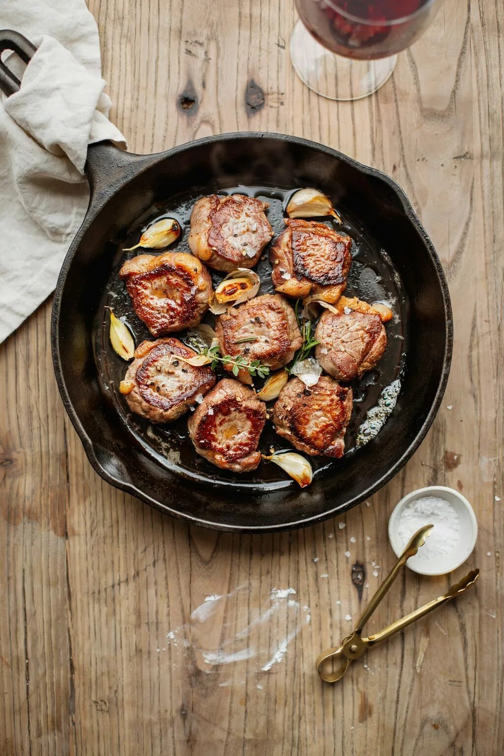 Small pieces of pork searing in a hot iron pan with garlic cloves and herbs.