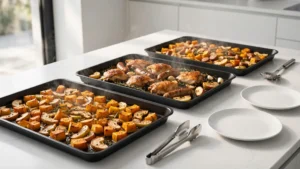 A rustic dining table covered in hot sheet pans filled with roasted fall vegetables and savory meats